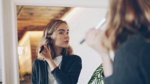 Young woman applying makeup in mirror Young woman applying makeup in mirror